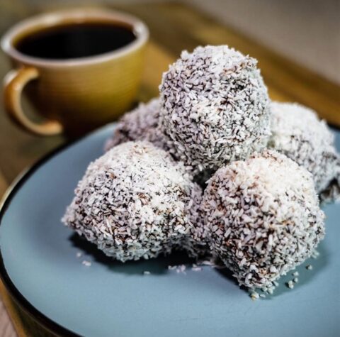 Chokladbollar med kokos på ett fat bredvid en kopp kaffe